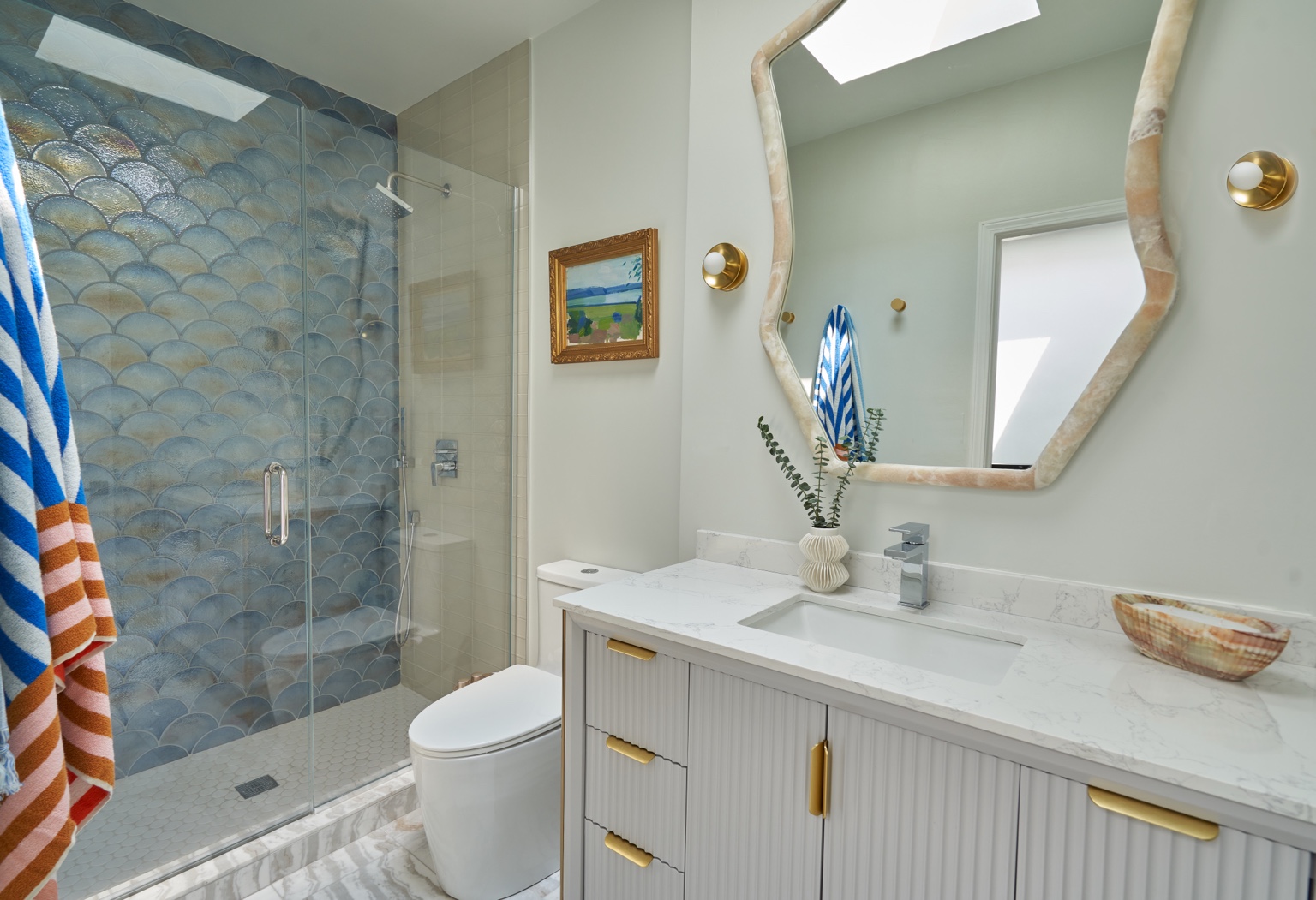 Blue scalloped shower tile beside the vanity, framed landscape and skylight