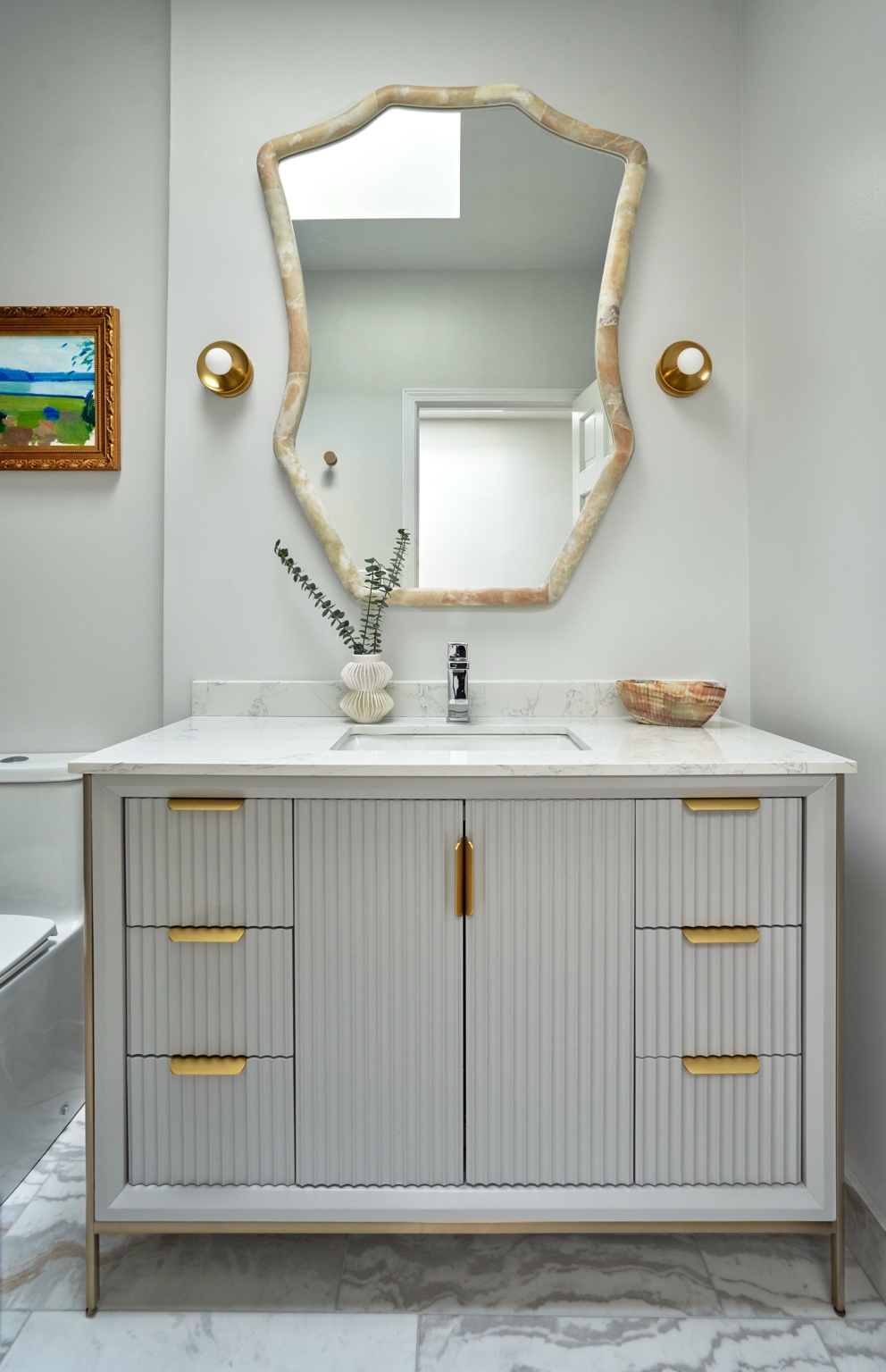 Pale ribbed vanity and sculptural mirror between two gold-toned globe sconces