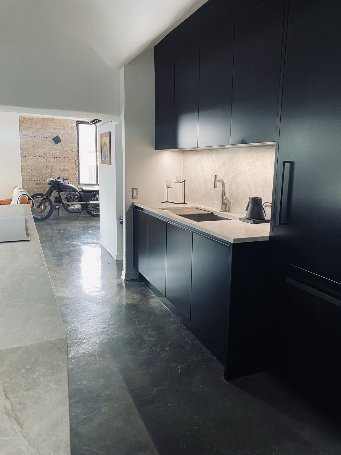 Dark full-height cabinetry beside the illuminated stone backsplash and sink
