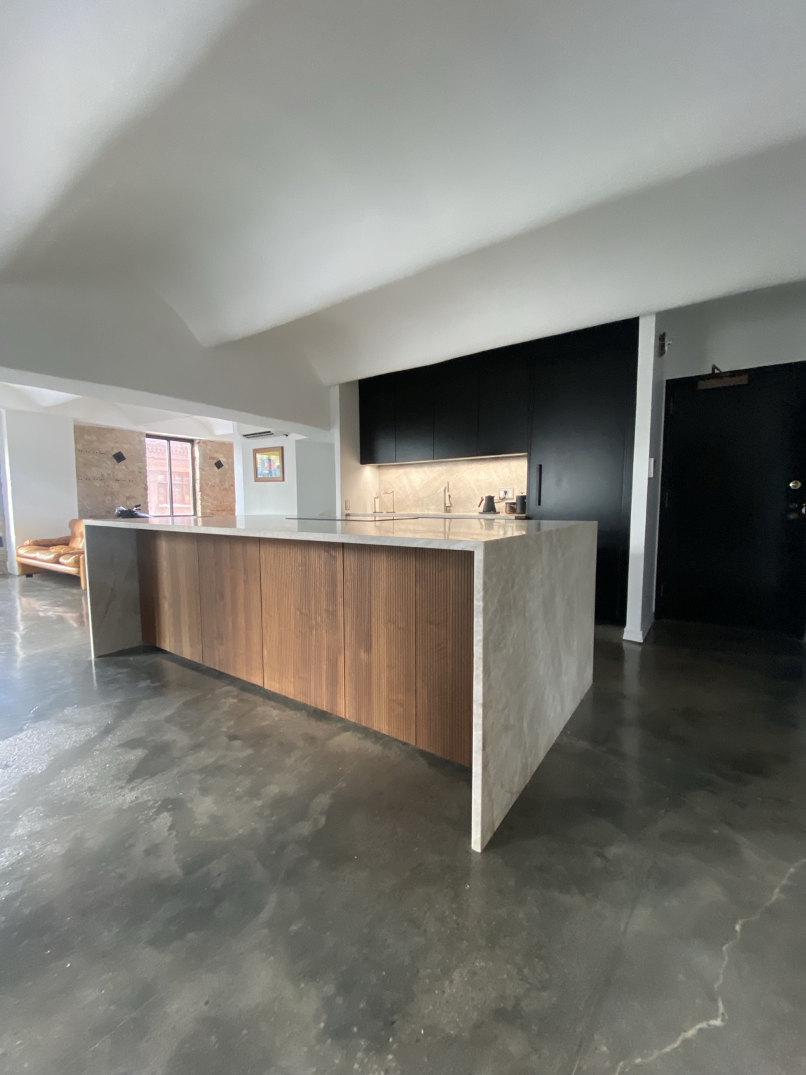 Angled view of the quartzite waterfall island and dark kitchen cabinetry