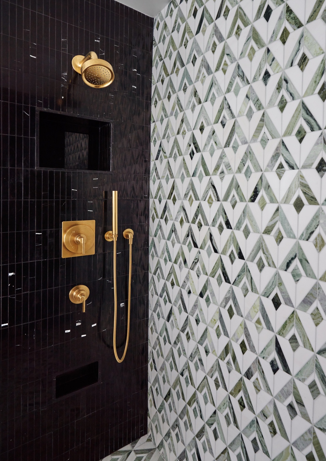 Gold-toned shower fittings against dark vertical tile beside the green and white geometric wall