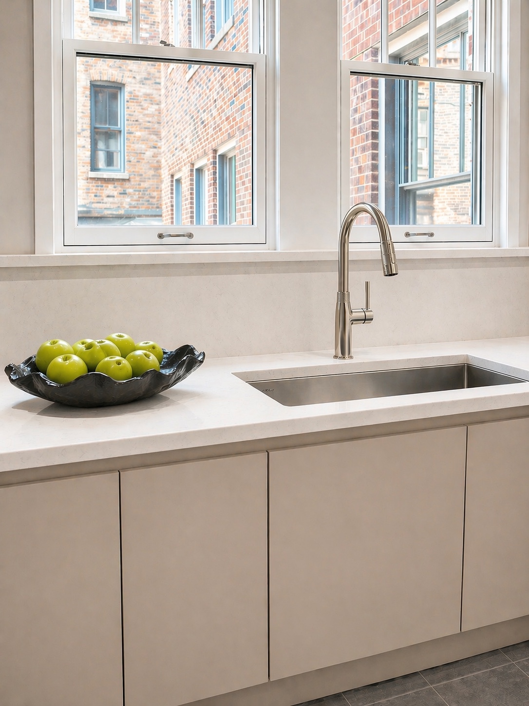 Kitchen sink beneath two windows with a bowl of green apples
